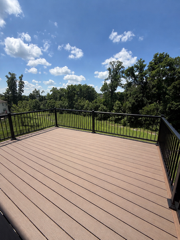 Composite deck boards with black metal railing and treeline view