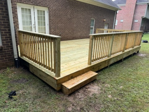 Large wood deck attached to a brick home with railing and step