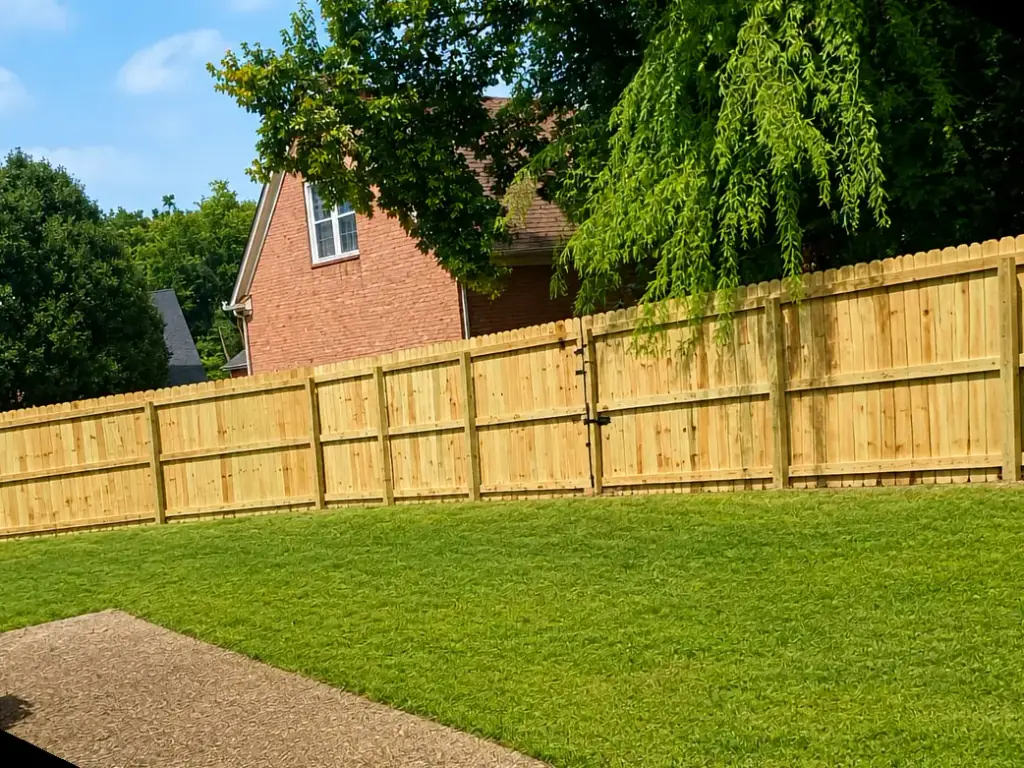 Board-on-board wood privacy fence with a gate section along a back lawn