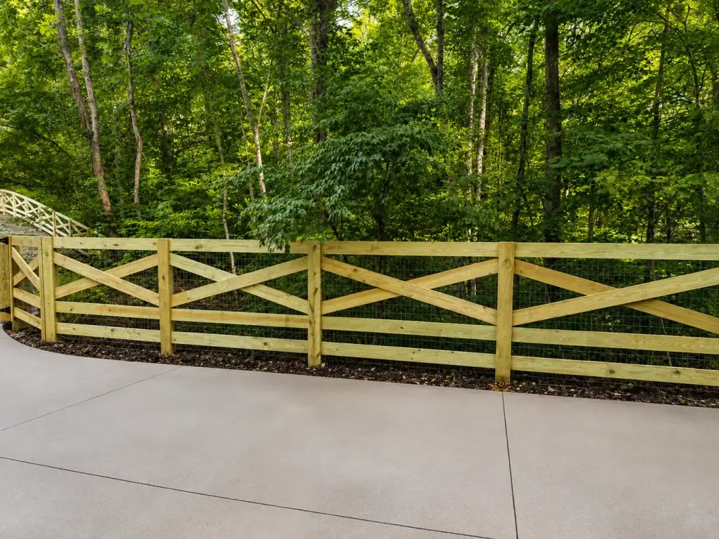 Wood ranch rail fence with wire mesh running along a concrete drive