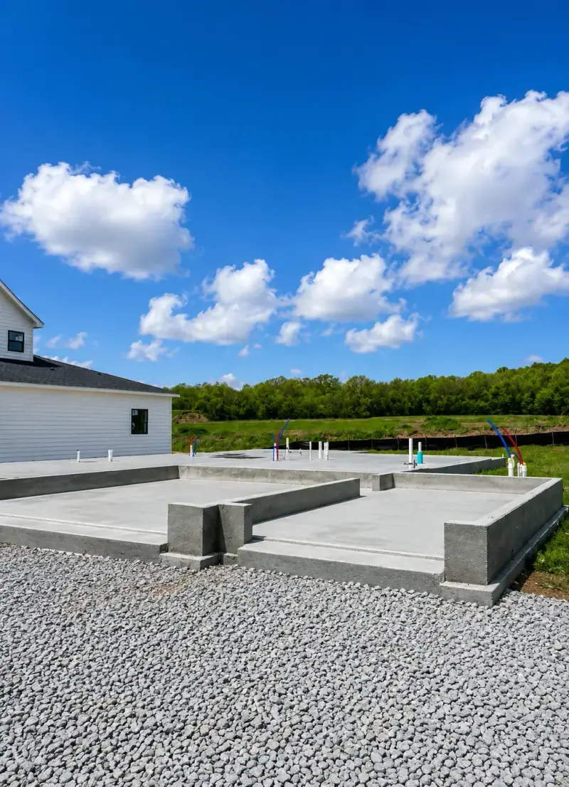 Poured concrete footings and slab on a gravel base under a blue sky