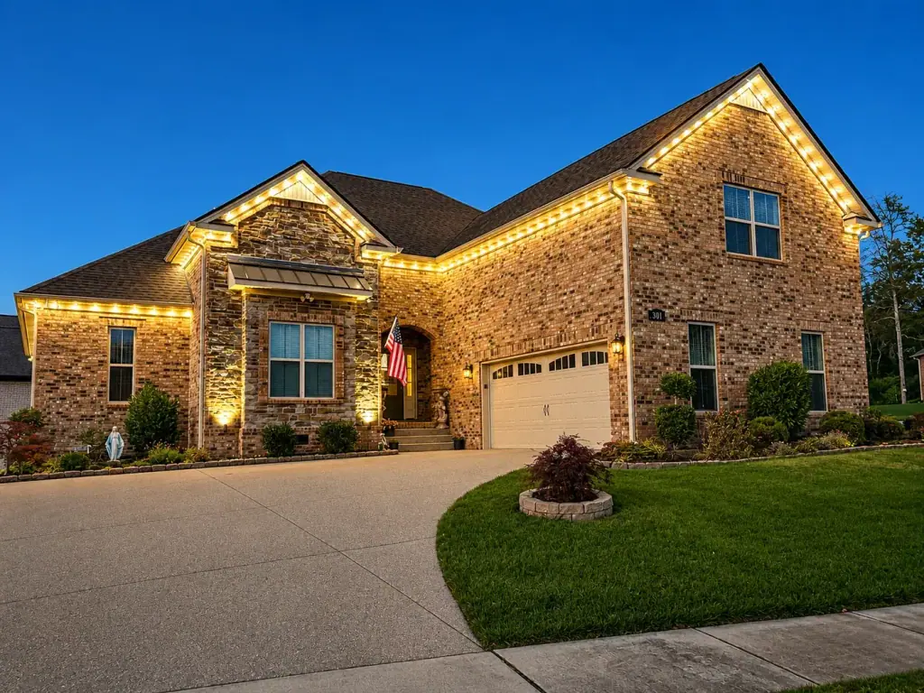 Stone and brick home outlined with warm white roofline lighting at dusk