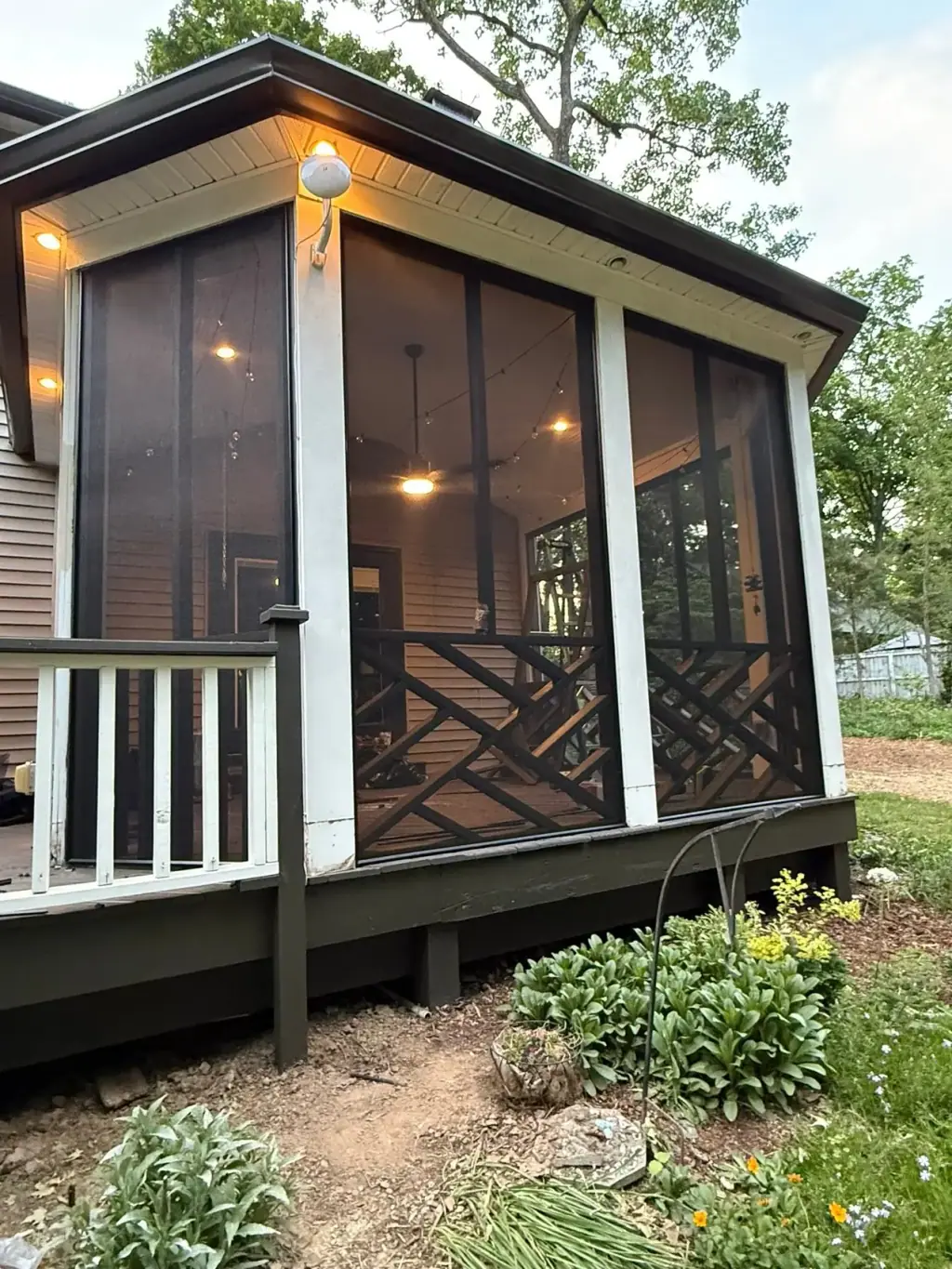 Screened porch with lattice detail and lights on at dusk